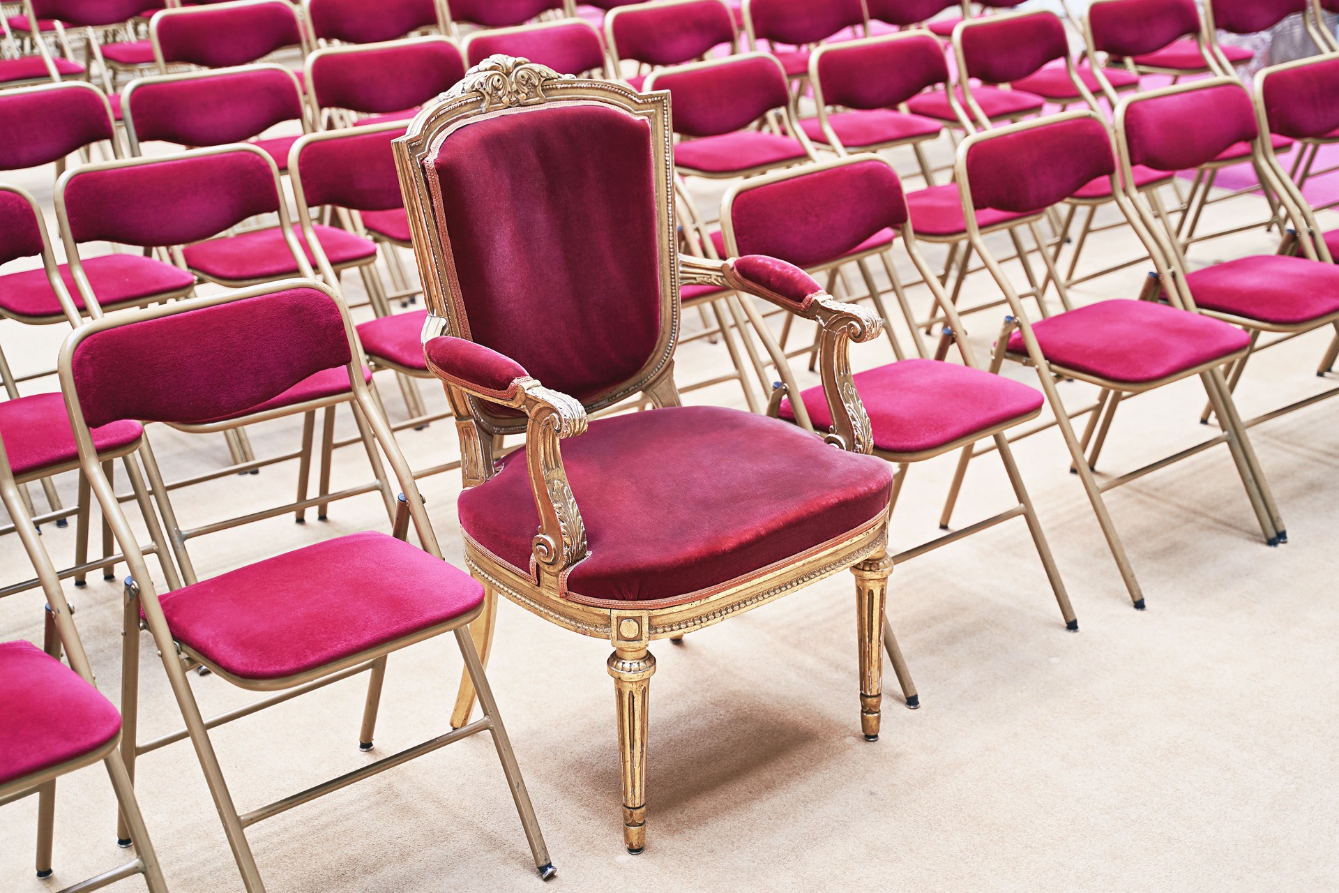 Unique throne or ceremonial armchair with velvet seat and golden details among many simple identical similar chairs. Uniqueness or exclusivity concept.
